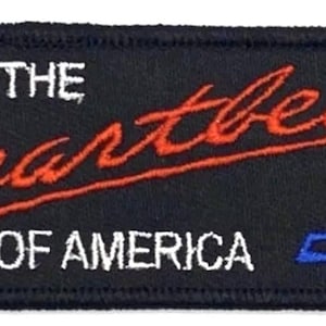 以下が含まれることがあります： 黒い長方形のパッチ。白と赤で「THE Heartbeat OF AMERICA」と刺繍されています。右側には青と白のシボレーのロゴがあります。パッチには黒い縁取りがあります。