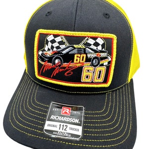 May include: Black and yellow trucker hat with a red, yellow, and black embroidered patch featuring a race car with the number 60 and the text "Winna Dixie". The patch also includes a signature. The hat has a black mesh back and a yellow brim. The hat has a label that reads "Richardson Original 112 Trucker Adjustable".