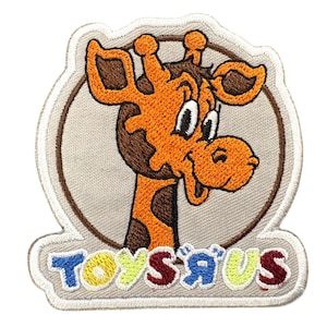 Könnte beinhalten: Ein gestickter Aufnäher mit dem Toys R Us Giraffen-Maskottchen in Orange und Braun vor einem kreisförmigen hellgrauen Hintergrund. Unter der Giraffe ist der Schriftzug Toys R Us in bunten Buchstaben auf einer hellgrauen Basis aufgestickt.
