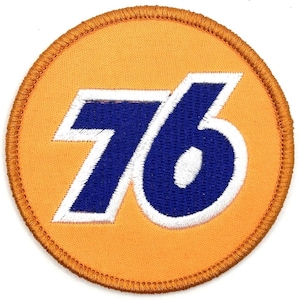 Pode incluir: Remendo redondo com o número "76" em azul com contorno branco, centrado em um fundo laranja. O remendo tem uma borda laranja costurada. O design lembra um logotipo vintage.
