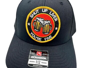 May include: Black trucker hat with a red, yellow, and white embroidered patch that says "Shut Up Liver You're Fine" with a graphic of two beer mugs.