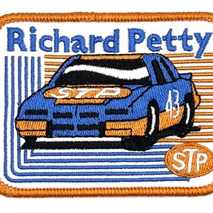 Puede incluir: Un parche bordado con un coche de carreras azul con el número 43 en el lateral. El coche está rodeado de rayas naranjas y azules y las palabras "Richard Petty" y "STP" son visibles.