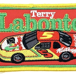 May include: A red, yellow, and green embroidered patch featuring a race car with the number 5 on the side. The car is sponsored by Kellogg's. The text "Terry Labonte" is above the car.