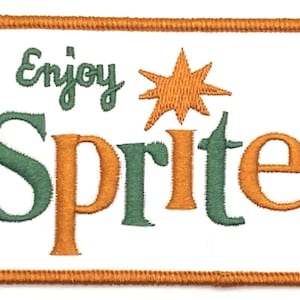 Pode incluir: Patch bordado com as palavras "Enjoy Sprite" em verde e laranja, com um gráfico de estrela. O patch tem um fundo branco e uma borda laranja.