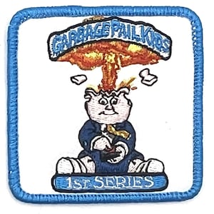May include: A white embroidered patch with a blue border. The patch features a cartoon character with a mushroom cloud exploding over their head. The text "GARBAGE PAIL KIDS" is above the character and "1ST SERIES" is below the character.