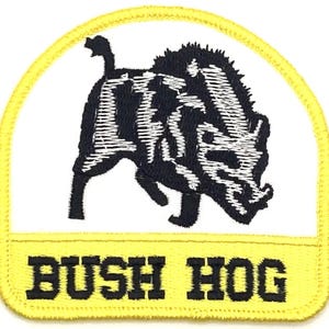 May include: Yellow and white embroidered patch featuring a black and white image of a wild boar and the text "BUSH HOG" in black.