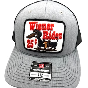 May include: Gray trucker hat with a black mesh back and a curved brim. The front features a patch with the words "Wiener Rides" and a cartoon dachshund. The hat also has a Richardson patch.