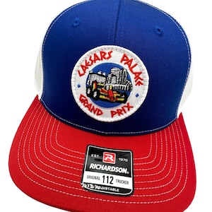 May include: A blue, white, and red trucker hat with a white patch featuring a logo that says "Lasars Palace Grand Prix" and a cartoon image of a go-kart. The hat is made by Richardson 112.