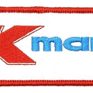 May include: Embroidered patch featuring the Kmart logo. The logo includes a red 'K' and blue 'mart' text, all within a white rectangle with a red border. The patch is designed for application on clothing or accessories.