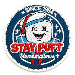 May include: Embroidered patch featuring the Stay Puft Marshmallow Man from the movie Ghostbusters. The patch is round with a blue background and white trim. Text includes "SINCE 1984" and "STAY PUFT Marshmallows".