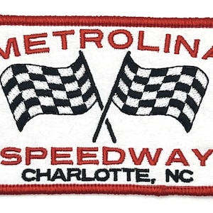Może przedstawiać: Naszywka haftowana na czerwono i biało z tekstem "Metrolina Speedway Charlotte, NC". Dwie szachownice są skrzyżowane w środku naszywki.