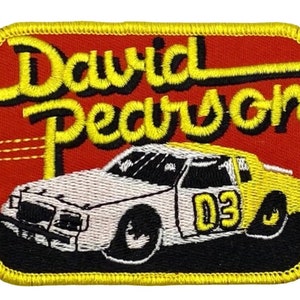 May include: A red, yellow, and white embroidered patch featuring a race car with the number 03 on the side and the text "David Pearson" above the car.