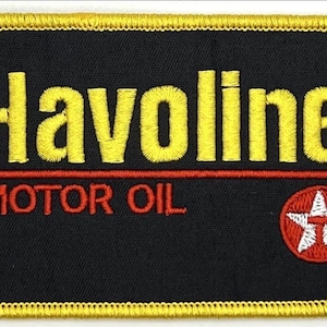 Pode incluir: Patch bordado com a palavra "Havoline" em amarelo, acima de "MOTOR OIL" em vermelho, sobre um fundo preto. Um logotipo de estrela vermelha e branca está no canto inferior direito. O patch tem uma borda amarela.