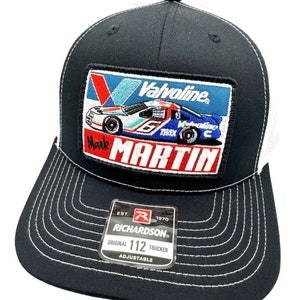 May include: Black and white trucker hat with a black and red embroidered patch featuring a race car with the text "Valvoline" and "Mark Martin". The hat has a white mesh back and a black front with a white stitched border. The hat has a black adjustable strap with a white label that reads "EST. 1970 RICHARDSON. ORIGINAL 112 TRUCKER ADJUSTABLE".