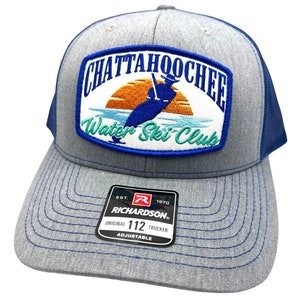 May include: A gray and blue trucker hat with a patch that says "Chattahoochee Water Ski Club" with a sunset and a person waterskiing. The hat is adjustable and has a Richardson logo.