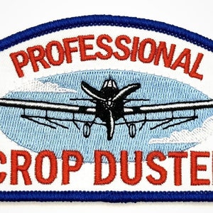 May include: A white embroidered patch with a blue border. The patch features a red airplane with the words "Professional Crop Duster" in red.