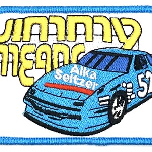 Puede incluir: Un parche bordado azul y blanco con un coche de carreras y el texto "Johnny Means" y "Alka Seltzer". El coche tiene el número 52 en el lateral.