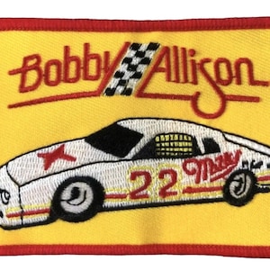 Peut inclure: Un écusson brodé jaune avec une bordure rouge représentant une voiture de course blanche avec le numéro 22 et le texte "Bobby Allison" en rouge.