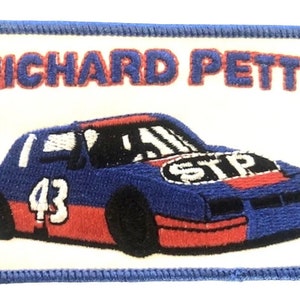 May include: Embroidered patch featuring a blue and red race car with the number 43. The patch has the text "RICHARD PETTY" above the car and the "STP" logo on the car. The patch is bordered with blue stitching.
