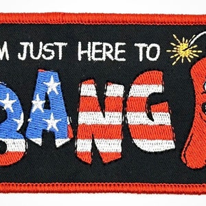 May include: An embroidered patch with a red border and black background. The text "I'm just here to" is in white. The word "Bang" is in red, white, and blue, resembling the American flag. A red, cartoon-like firecracker with a face is on the right side of the patch.