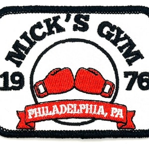 Può includere: Toppa ricamata bianca con cuciture nere. La toppa presenta un design di guantoni da boxe rossi con il testo "Mick's Gym 1976 Philadelphia, PA".