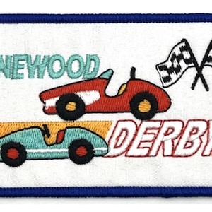 May include: A white embroidered patch with a blue border featuring two toy race cars, one red and one blue, with the text "Pinewood Derby" in green and red.