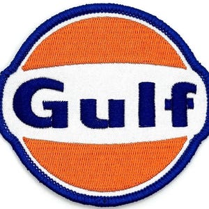 Puede incluir: Parche bordado con el logotipo de Gulf Oil. El parche tiene un fondo blanco con un diseño ovalado naranja y azul. La palabra "Gulf" está bordada en azul, con un borde azul.