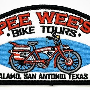 May include: Embroidered patch with a black border, featuring a red bicycle with a blue oval behind it. The text "Pee Wee's Bike Tours" is in red and black lettering. The text "Alamo San Antonio Texas" is in black lettering.