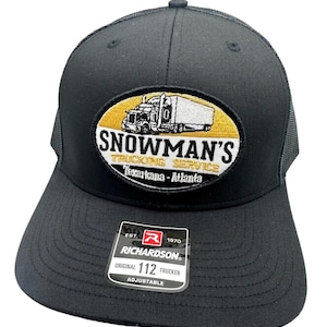 May include: Black trucker hat with a curved brim and mesh back. The front features an embroidered patch with the text "SNOWMAN'S TRUCKING SERVICE Texarkana - Atlanta" and an image of a semi-truck. The hat is adjustable.