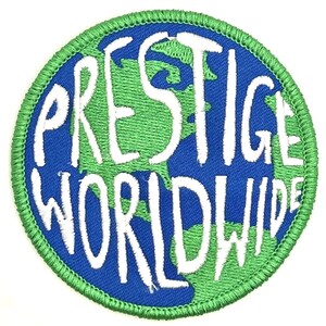 May include: A green and blue embroidered patch with the text "Prestige Worldwide" in white.
