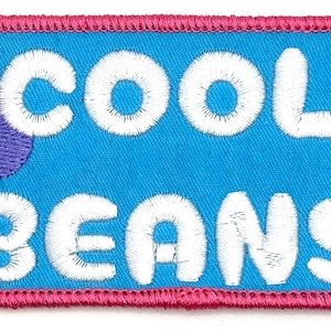 May include: A blue and pink embroidered patch with white lettering that reads "COOL BEANS". There is a purple and pink embroidered design in the upper left corner.