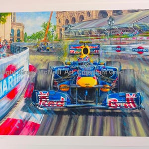May include: A vibrant painting of a blue and yellow Red Bull Formula One race car speeding along a city street circuit. The scene features Martini branding on the trackside barriers, a photographer on the sidelines, and a second car in the distance.