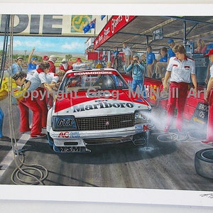 May include: A red and white racing car with the words "Commodore" and "Marlboro" on the side. The car is being worked on by a team of mechanics in red and white uniforms. The car is in a pit stop area with a crowd of people in the background.