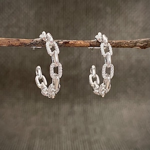 May include: A pair of silver hoop earrings with a chain link design. The earrings are adorned with small, clear stones.