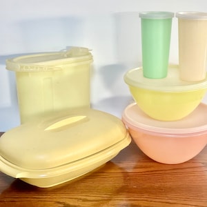 Può includere: Un set di contenitori per la conservazione degli alimenti in plastica gialla e pesca con coperchi. I contenitori sono impilati uno sopra l'altro. I contenitori sono di diverse dimensioni.