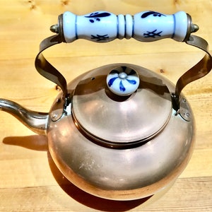 Peut inclure: Une bouilloire en cuivre avec une poignée et un bouton de couvercle en porcelaine blanche. La poignée et le bouton sont décorés de motifs floraux bleus.