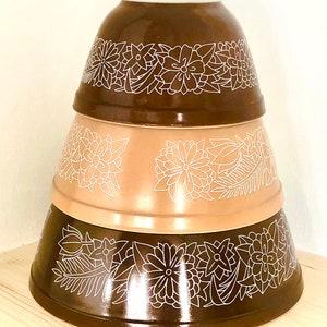 Pode incluir: Um conjunto de três tigelas de mistura castanhas e bege com um design floral branco. As tigelas estão empilhadas umas sobre as outras.