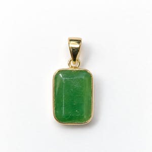 May include: A rectangular pendant featuring a faceted green gemstone set in a polished gold-toned metal frame. The pendant includes a matching gold-toned bail at the top, designed for attachment to a necklace chain or cord.
