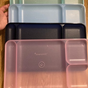 May include: Four plastic divided serving trays in different colours: light green, light blue, dark blue, and pink. The pink tray has the word "Tupperware" printed on it.