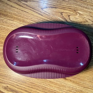 May include: A burgundy plastic container with a textured rim and the word "Tupperware" printed on the bottom.