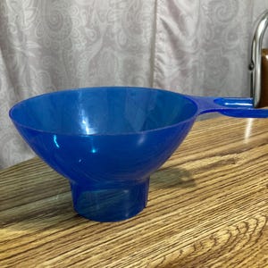 May include: A blue plastic funnel with a handle. The funnel is on a wooden surface.