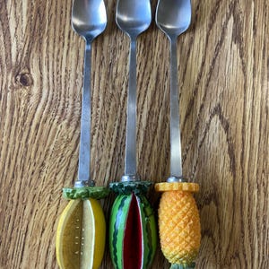 May include: Three silver spoons with fruit-shaped handles. The handles are a lemon, watermelon, and pineapple.