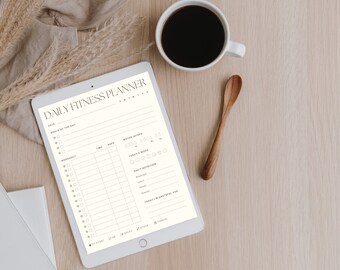 Op de afbeelding: Een witte tablet met een dagelijkse fitnessplanner-app geopend. De app heeft secties voor datum, doelen van de dag, training, tijd, herhalingen, waterinname, stemming van vandaag, dagelijkse voeding en vandaag ben ik dankbaar voor. De tablet ligt op een lichtbruin houten oppervlak met een witte koffiemok en een houten lepel.