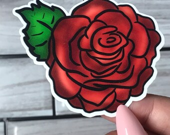 May include: A red rose sticker with a black outline and a green leaf. The rose has a detailed design with shading to give it a realistic look. The sticker is on a white background.