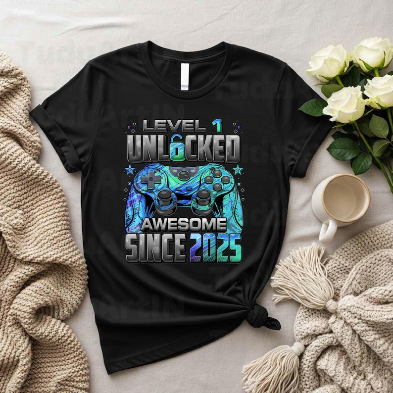 Pu&ograve; includere: T-shirt nero con grafica di un controller di videogiochi blu e verde. Il testo recita "LEVEL 1 UNLOCKED AWESOME SINCE 2025". La maglietta &egrave; annodata in vita. Abbigliamento casual.