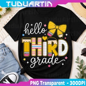 Pode incluir: Uma t-shirt preta de manga curta com um design gráfico que inclui o texto hello THIRD grade. O design apresenta um laço amarelo em forma de lápis, um coração amarelo e estrelas coloridas. As letras imitam papel pautado e lápis.