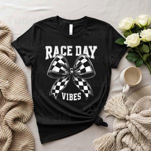 Może przedstawiać: Czarny t-shirt z białym napisem "RACE DAY VIBES". Duża kokarda z wzorem szachownicy znajduje się na środku. Koszulka jest zawiązana na dole.