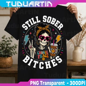 May include: A black t-shirt featuring a graphic of a skeleton wearing heart-shaped sunglasses and a leopard print headband. The skeleton holds a coffee cup and makes a peace sign. Text reads STILL SOBER BITCHES and CHOOSE PEACE with a smiley face.