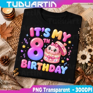 Puede incluir: Una camiseta negra con un gráfico colorido que incluye el texto IT'S MY 8TH BIRTHDAY en letras de burbuja. El diseño muestra un personaje de dibujos animados rosa dentro de una caja de regalo decorada, rodeado de estrellas, corazones y confeti.