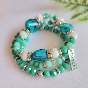 May include: A multi-strand bracelet with green and white beads and a silver charm that says "Dream".